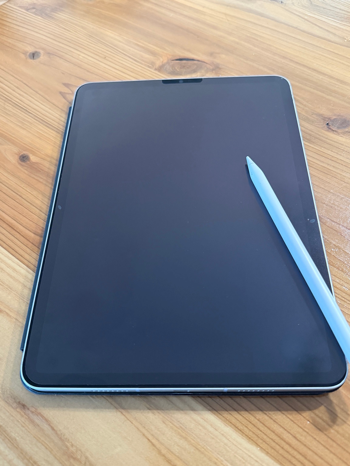 木の机に置いたペーパーライクフィルム付きのiPadと白いペン